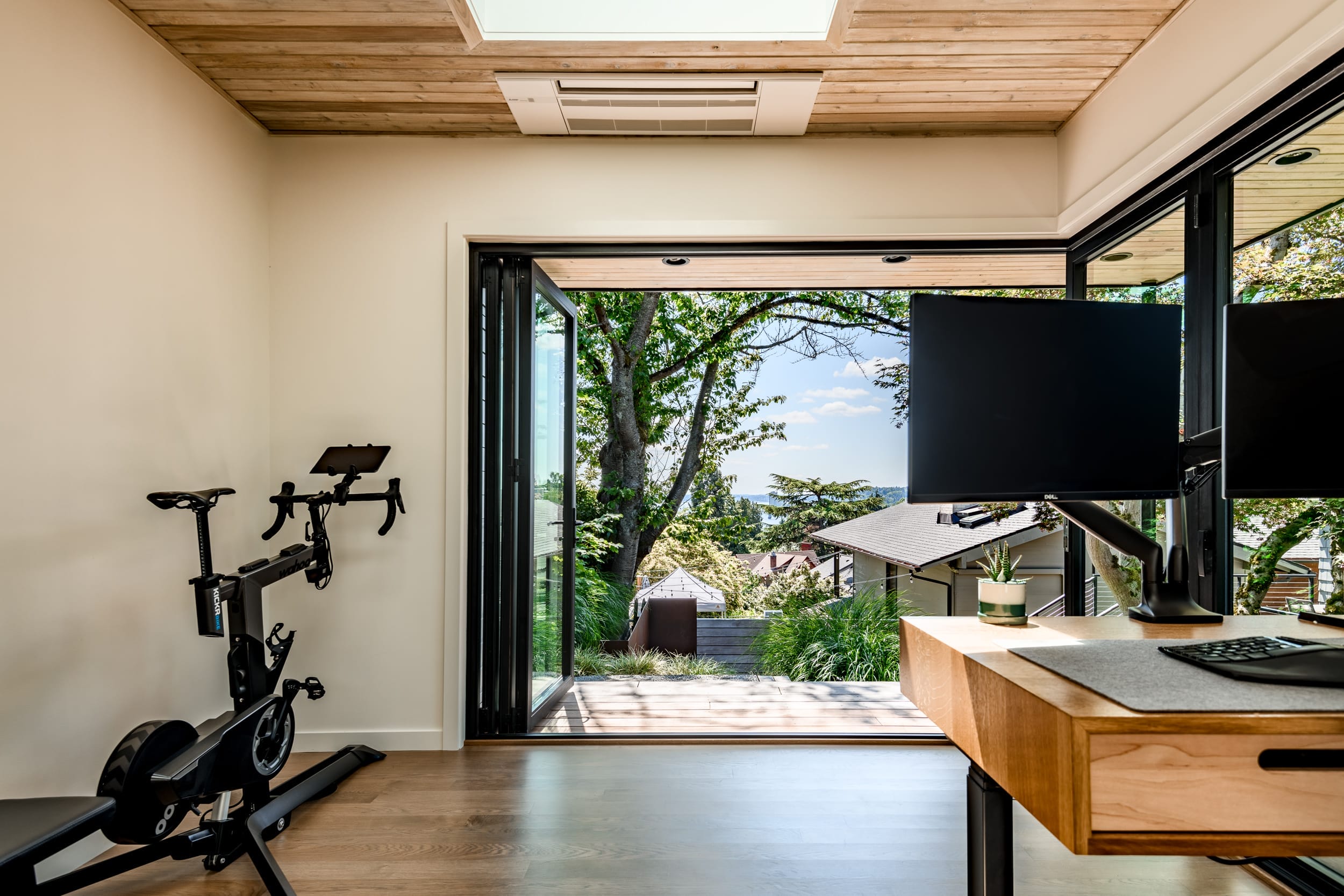 A room with a desk and a computer and a bike.