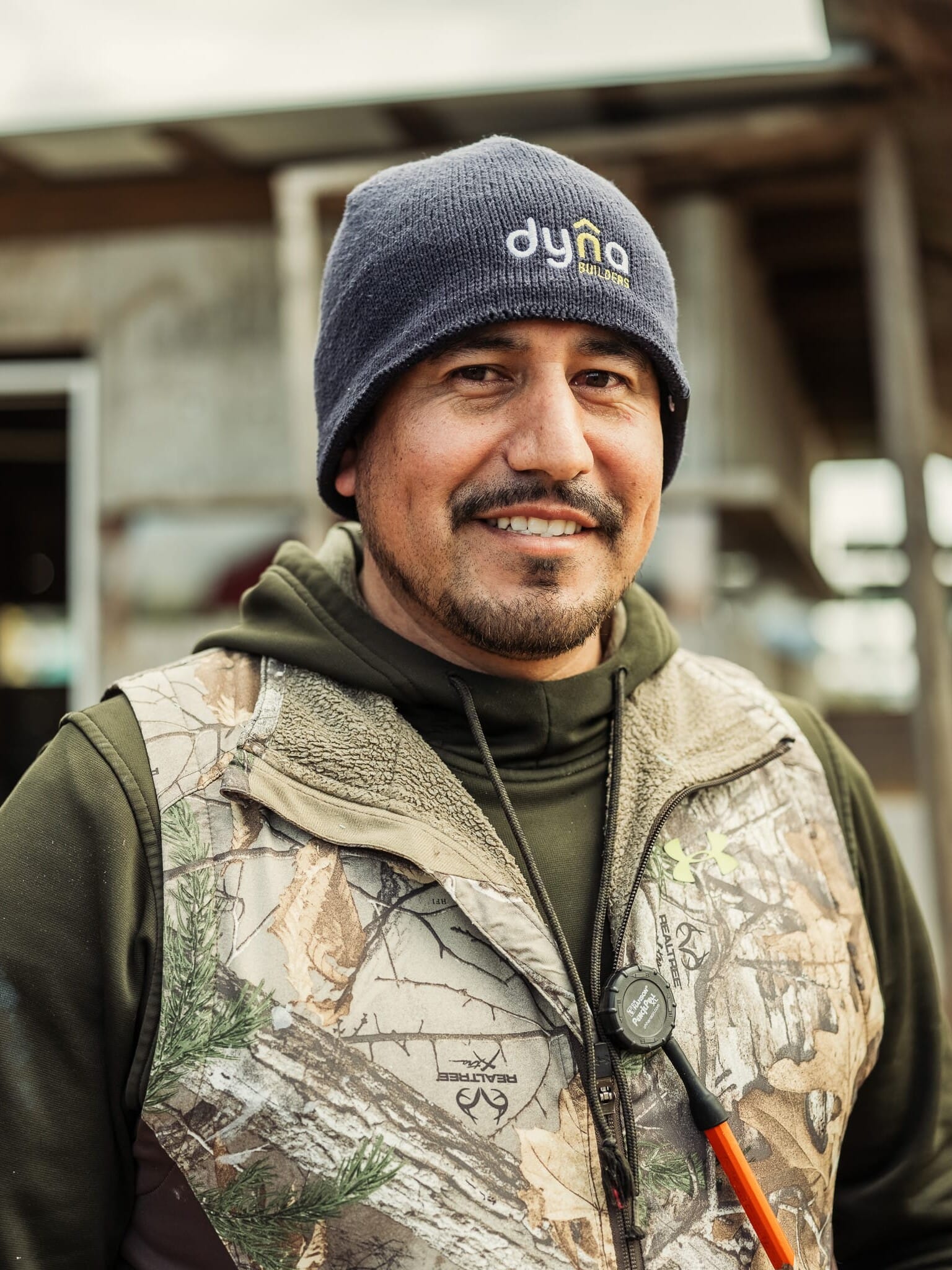 Abel Guzman, a man wearing a camouflage vest and hat, works as a carpenter for Dyna Builders.