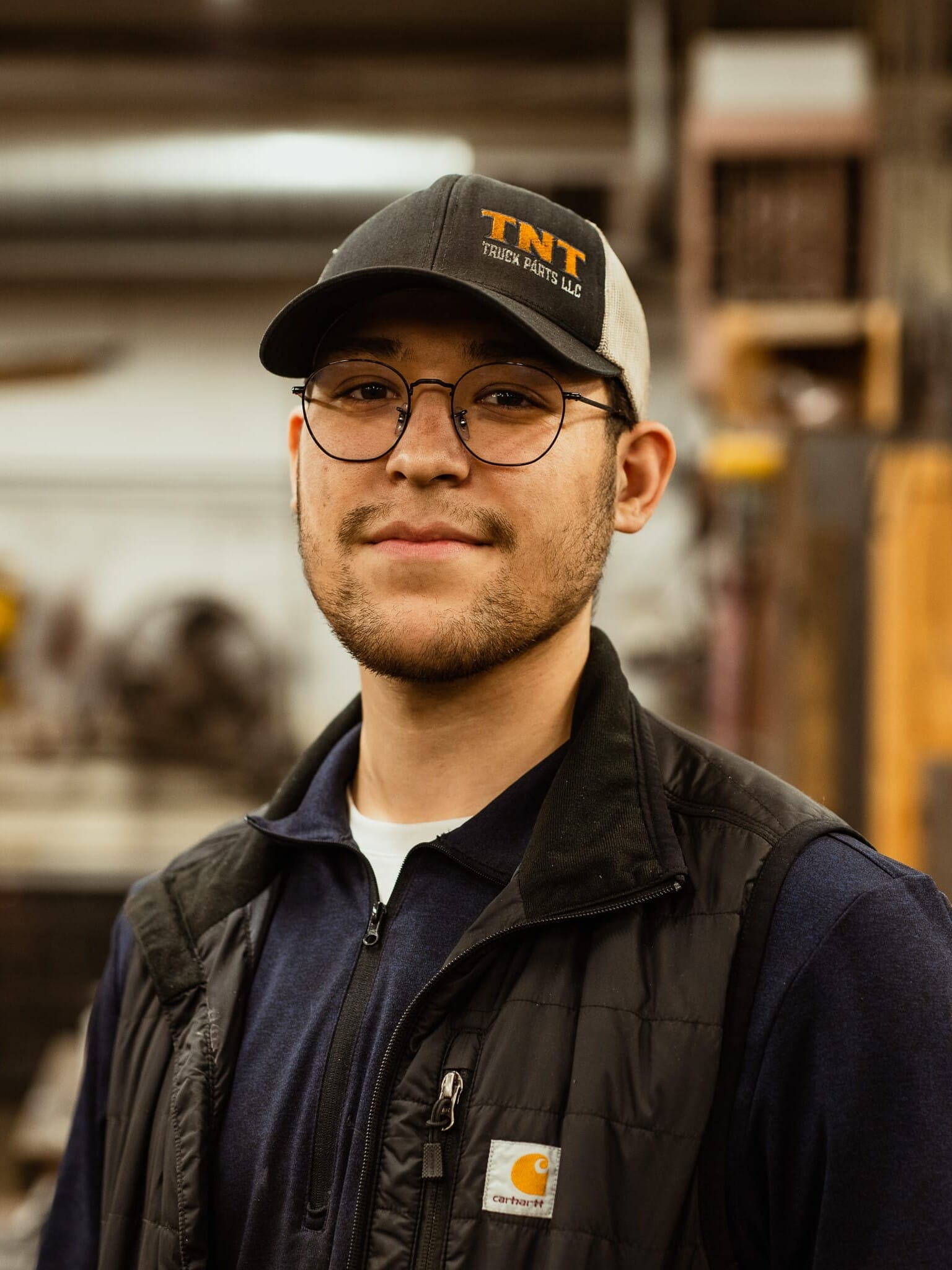 A man wearing glasses and a hat in a factory.