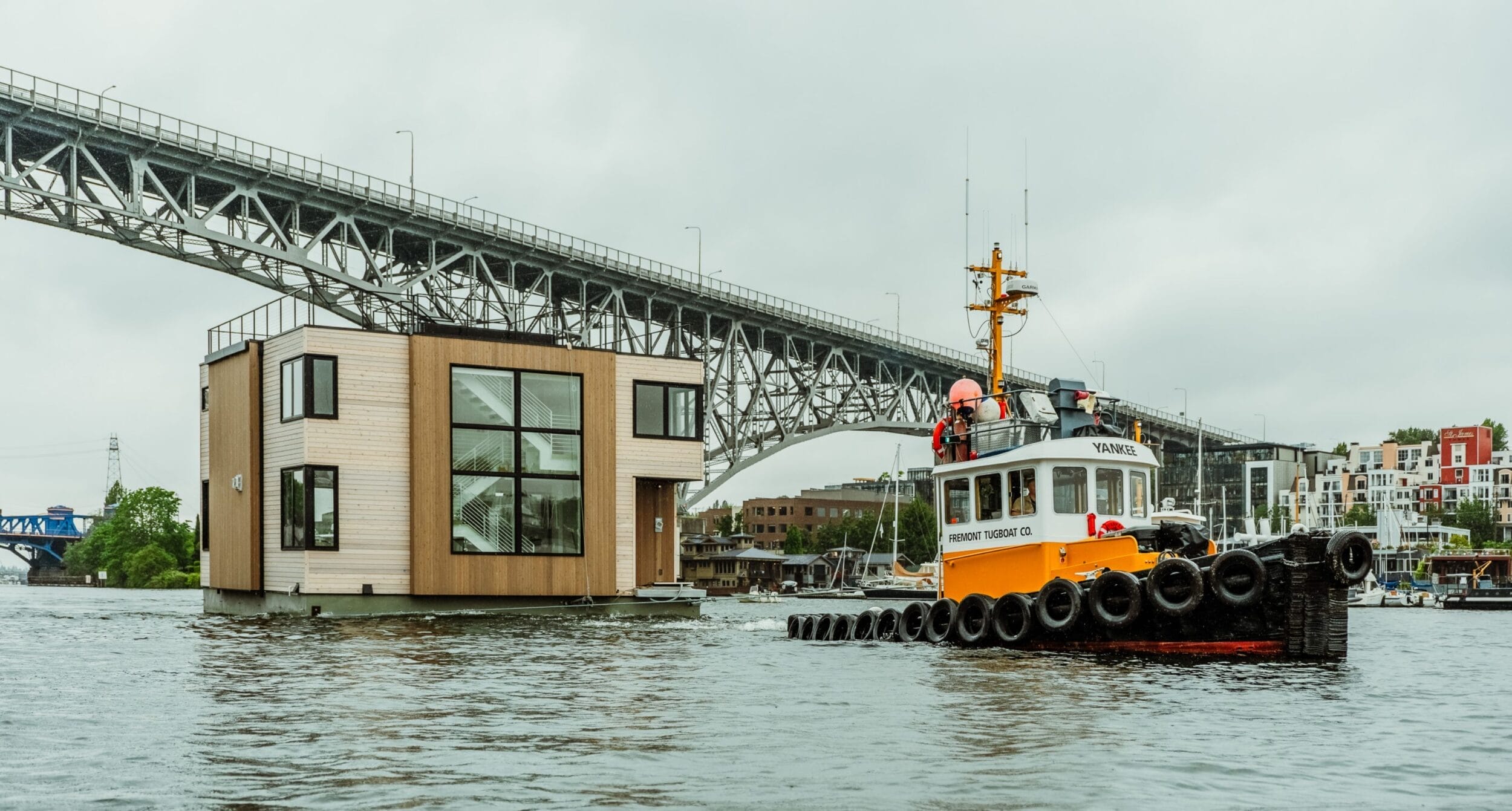 A Dyna floating home, built by Dyna Builders, peacefully floats in the water under a bridge.