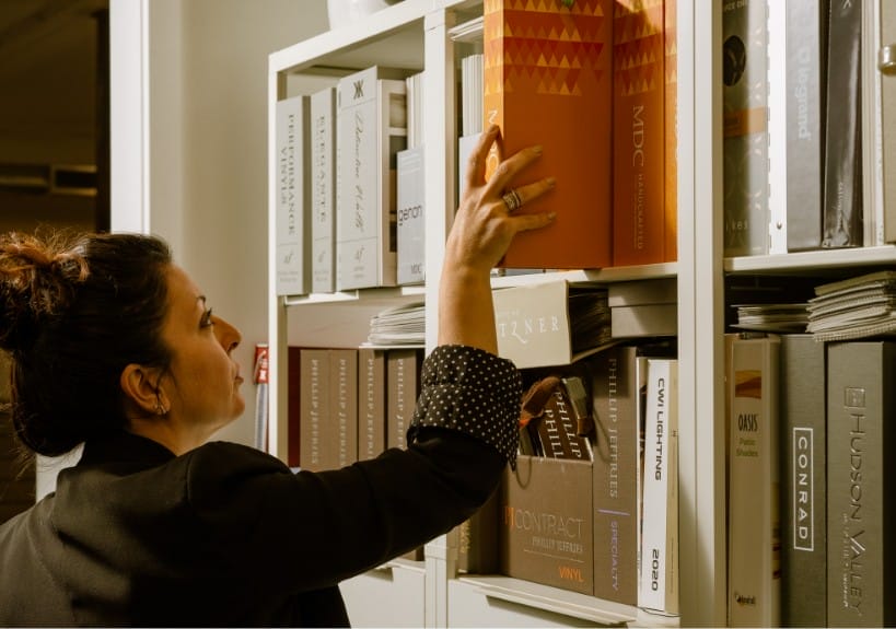 A woman reaching for a folder on a shelf in a Seattle based custom home builder's office.