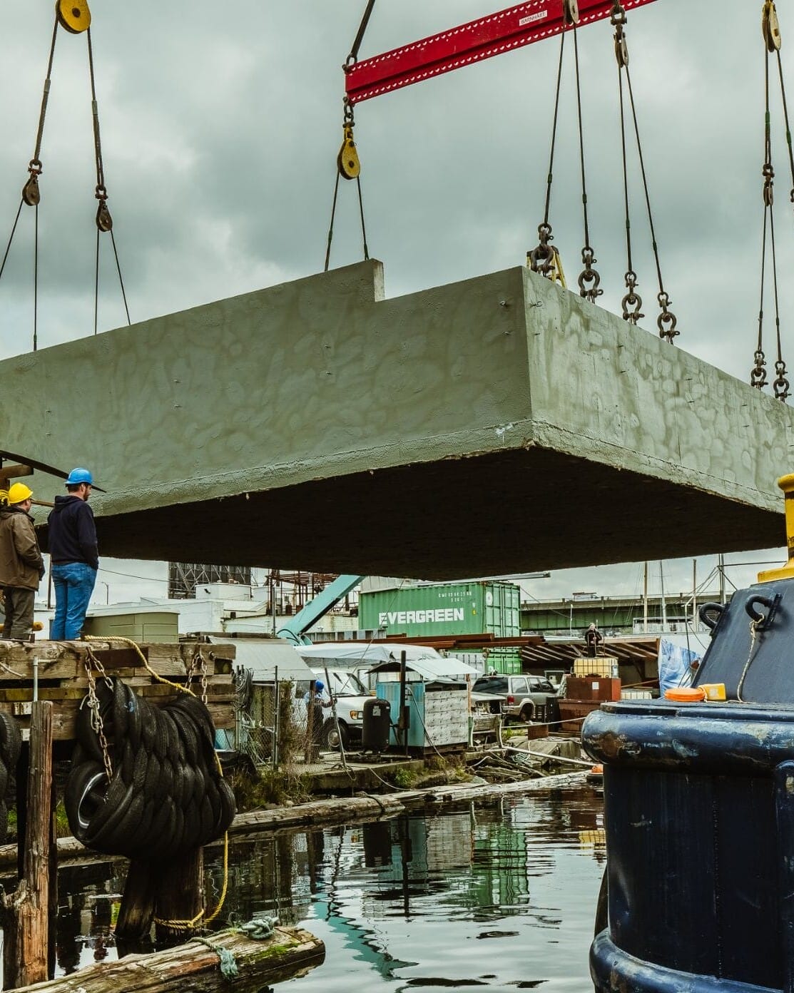 A Floating Homes Contractor is using a crane to lift a large concrete block onto a boat.