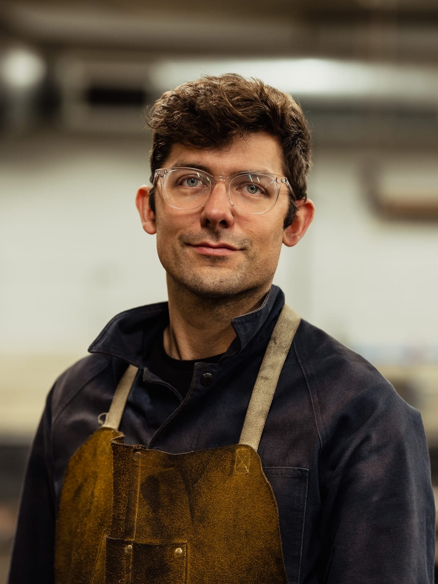 A man wearing glasses and an apron in a workshop.