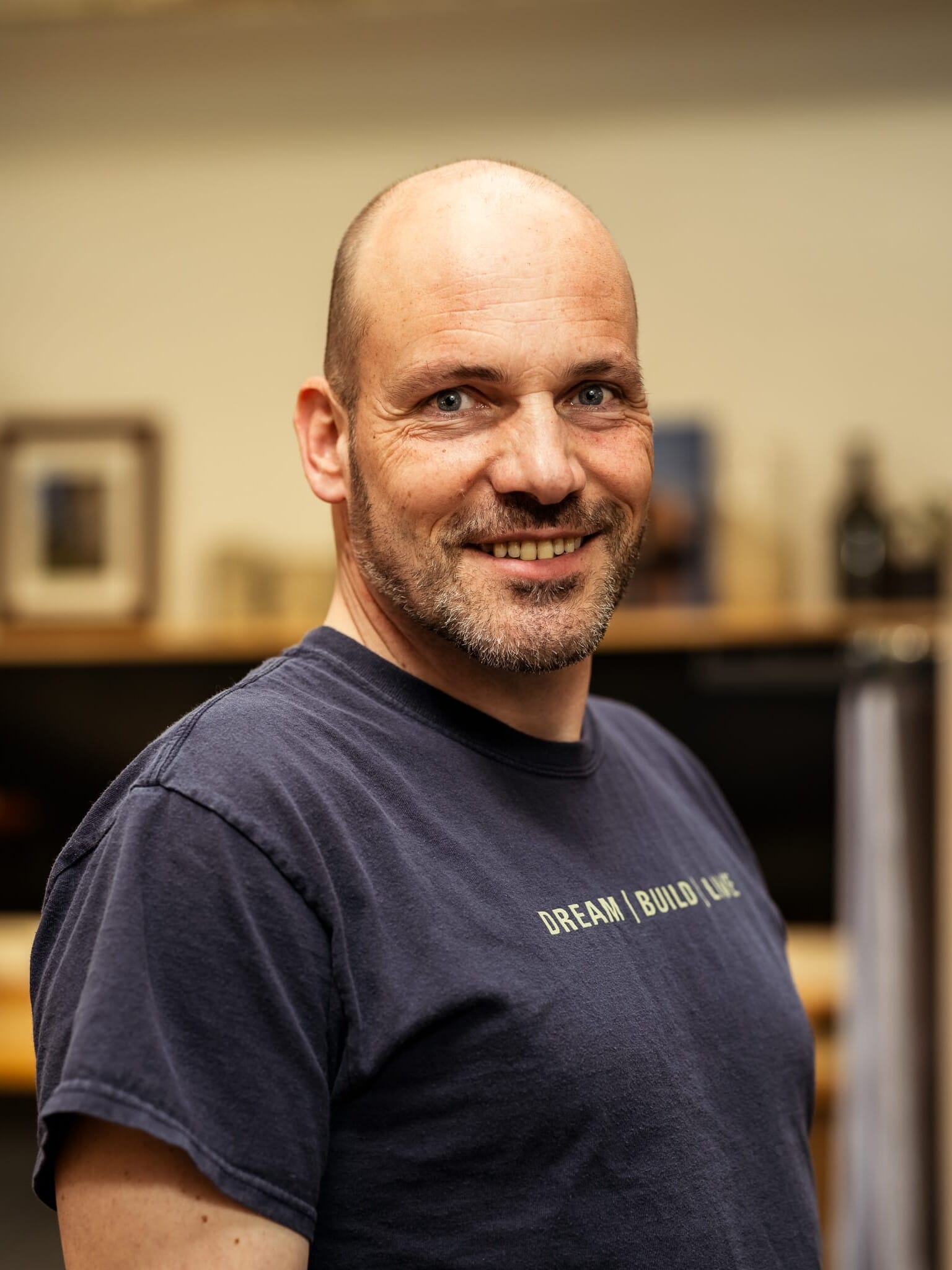 A bald man in a blue t - shirt smiling.