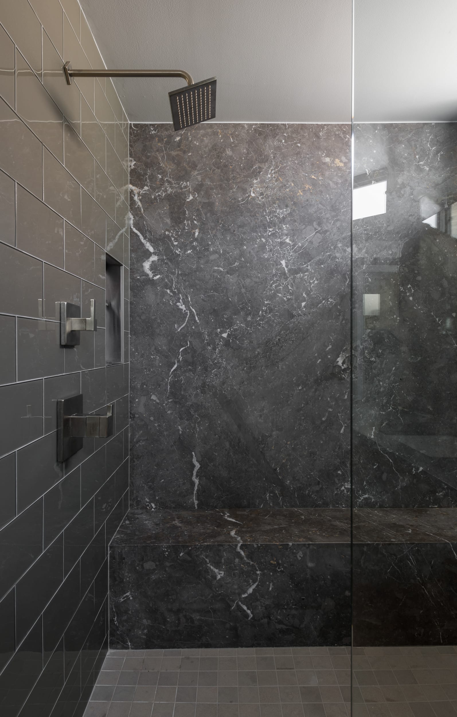 A modern bathroom with a glass shower stall and black marble walls.