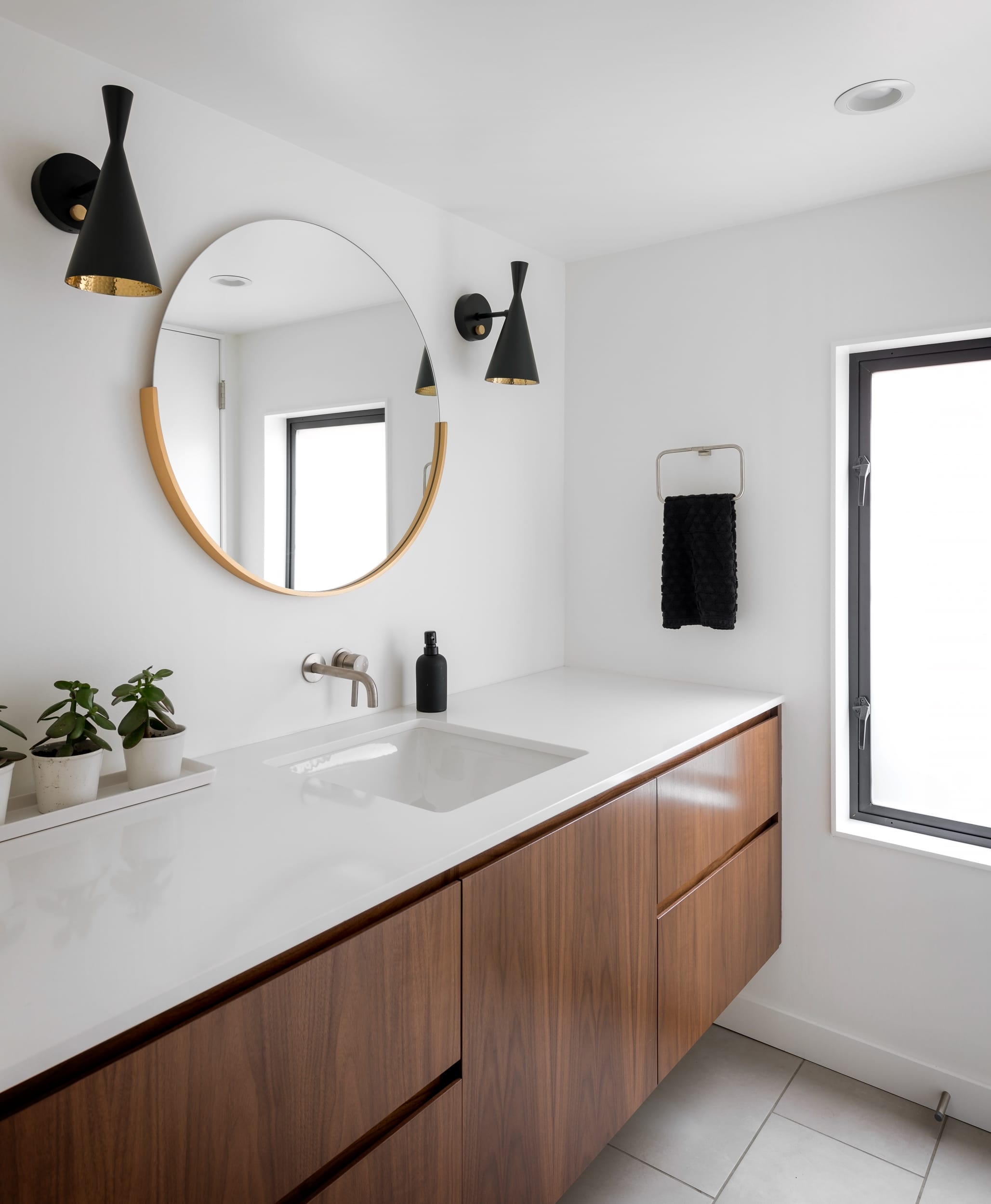 A modern bathroom with wooden cabinets and a round mirror.