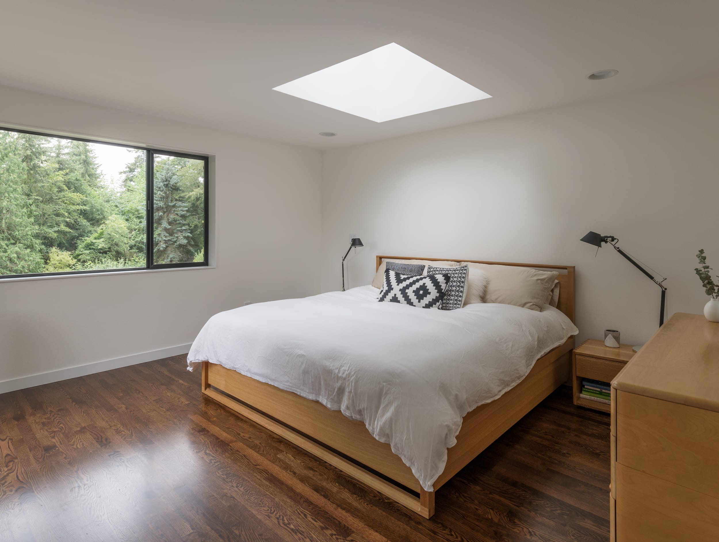 A bedroom with a skylight and hardwood floors.