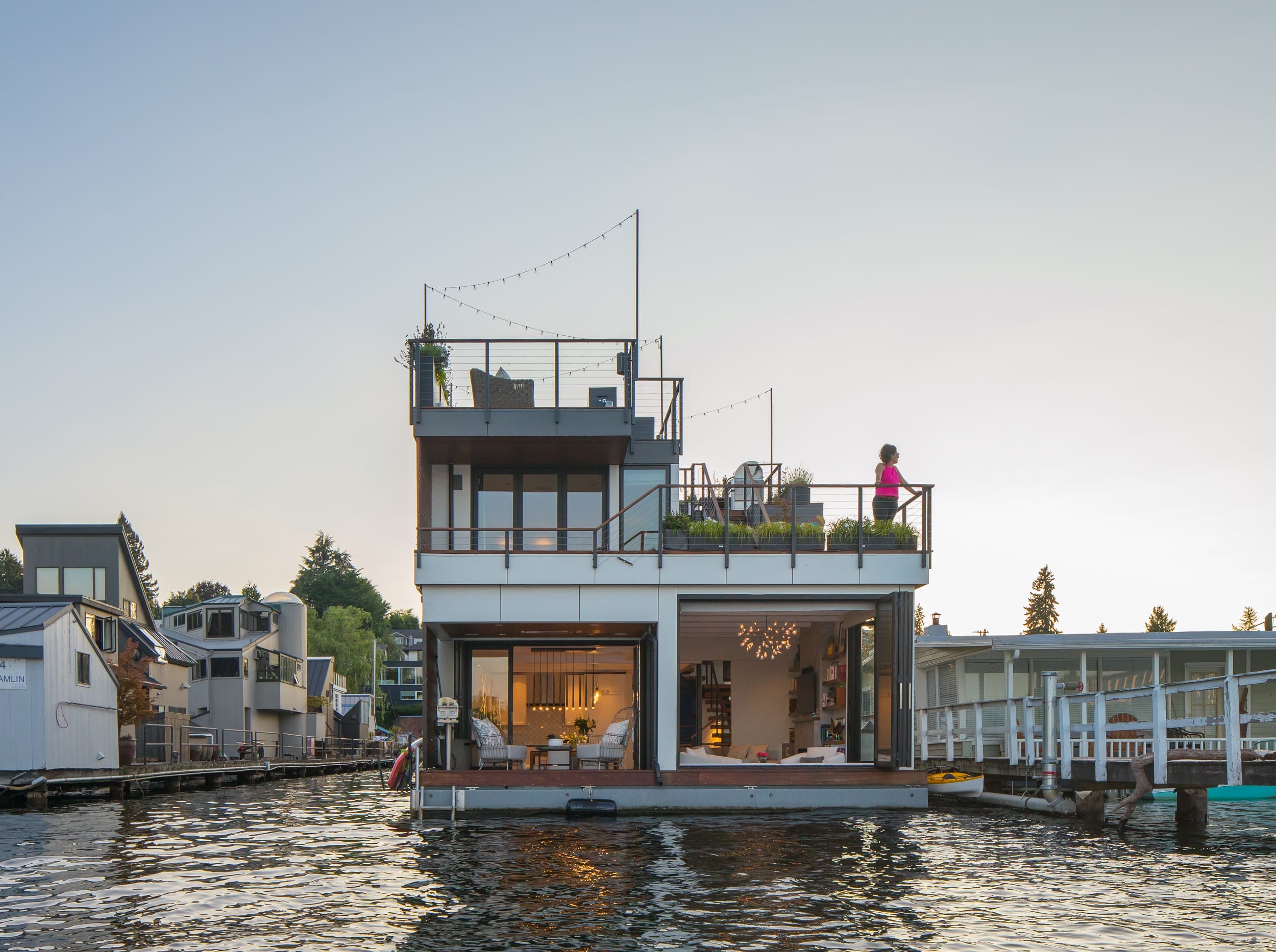 A modern houseboat designed and built by a skilled carpenter, floating on the water with a person enjoying the view from the top.