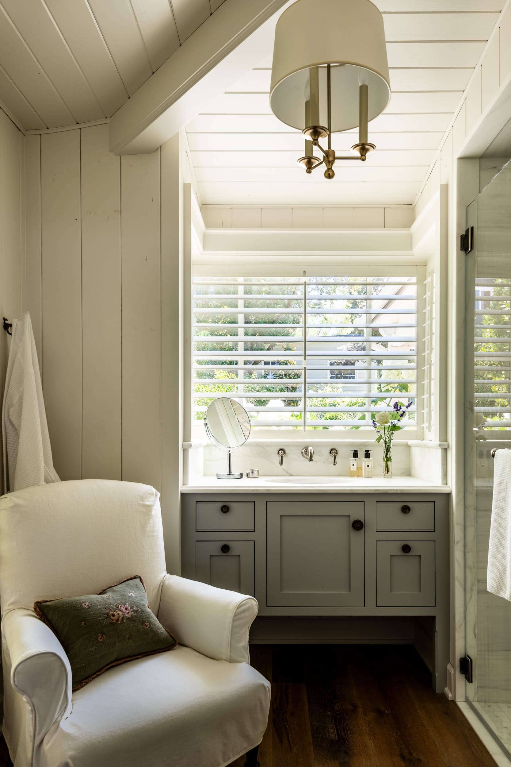 A bathroom with a white chair and a window.