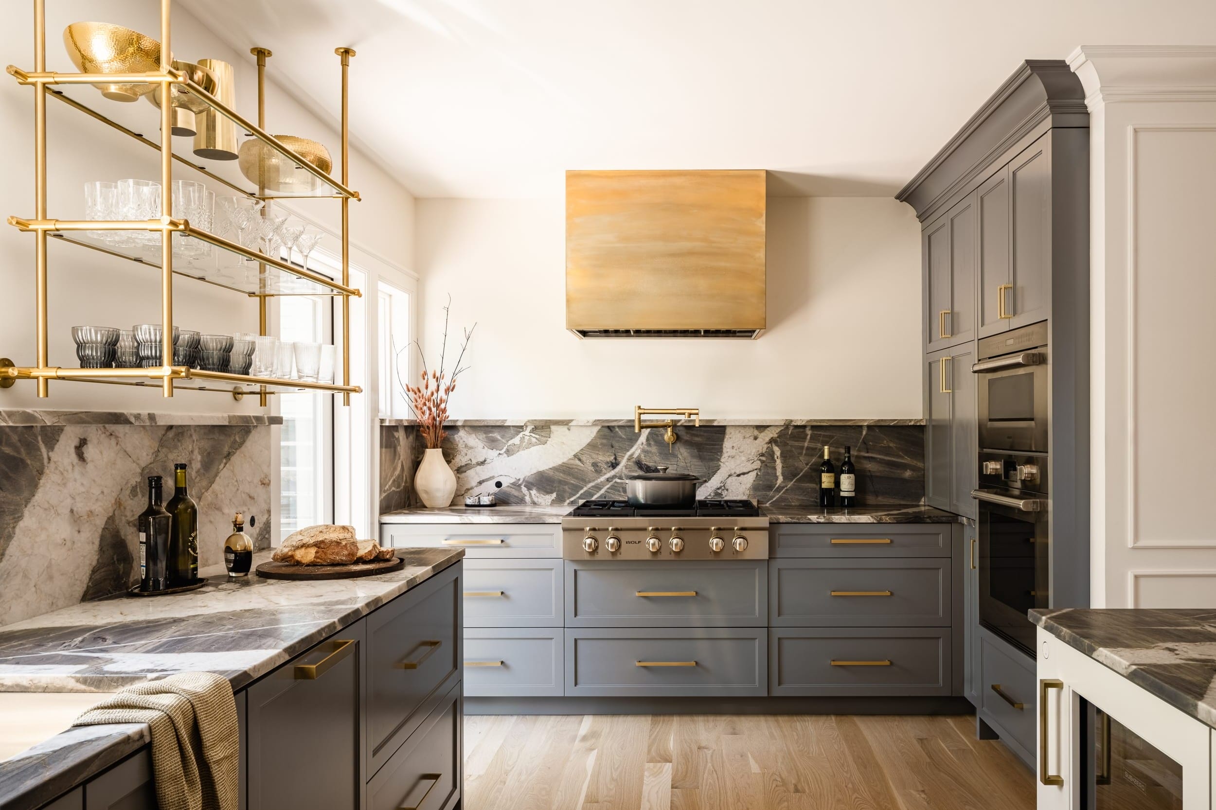 A gray and gold kitchen with marble counter tops.