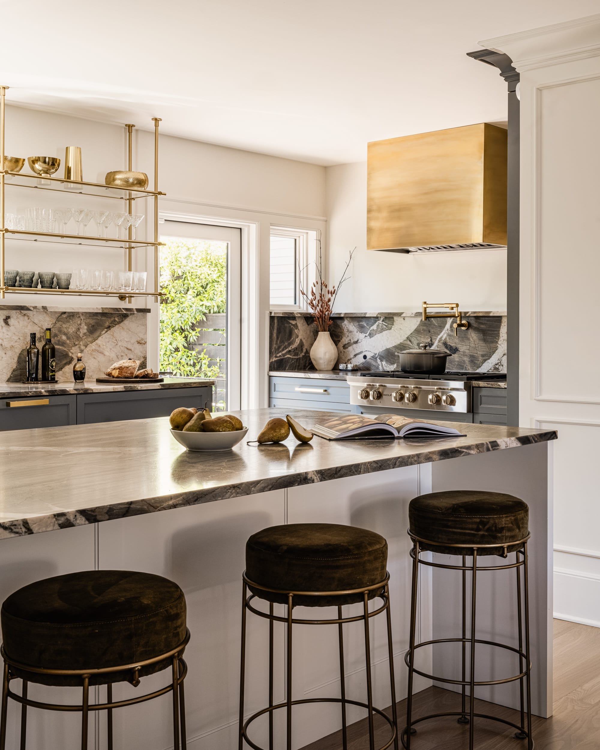 A kitchen with a marble counter top and gold stools.