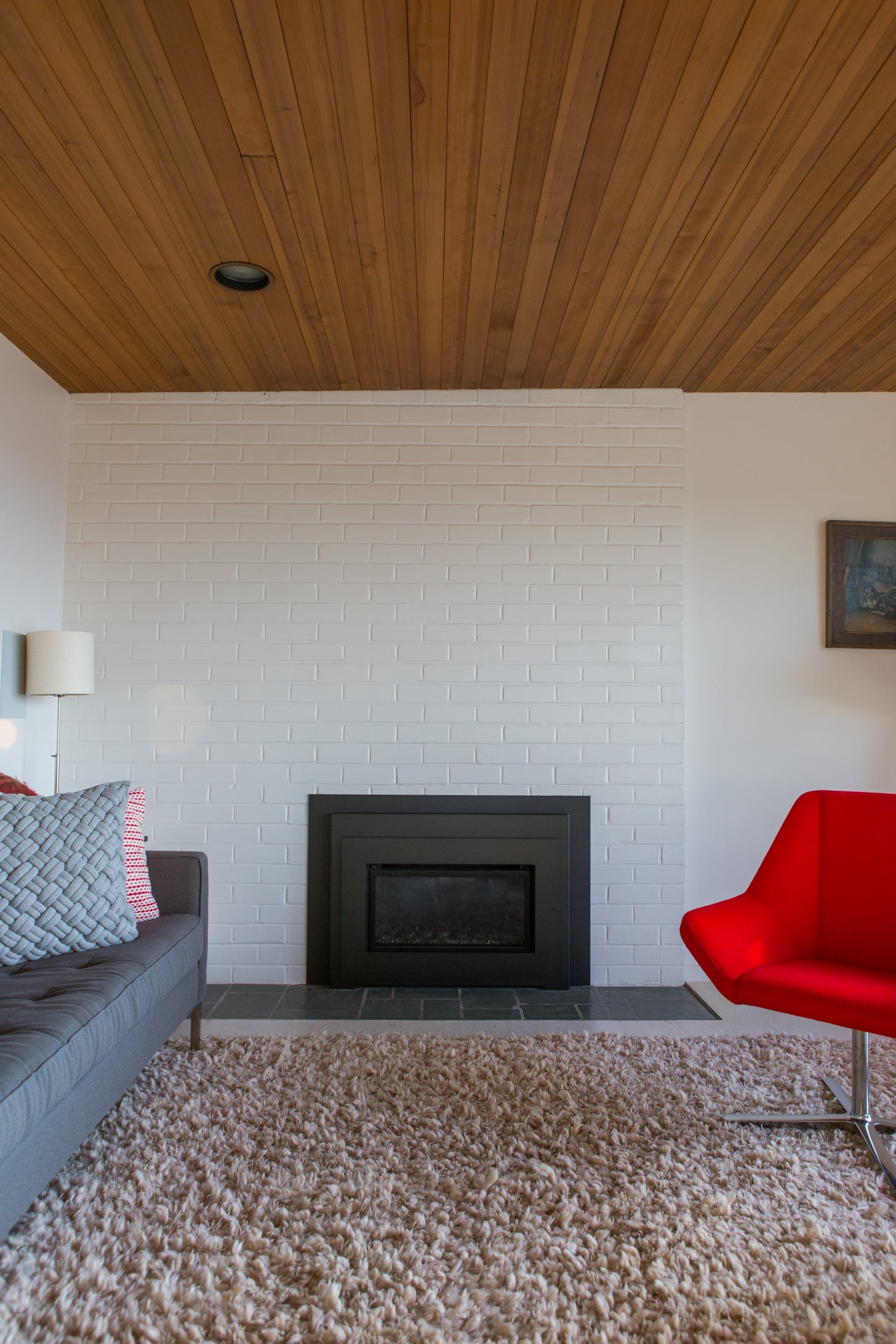 A living room with a wood ceiling and red chair.