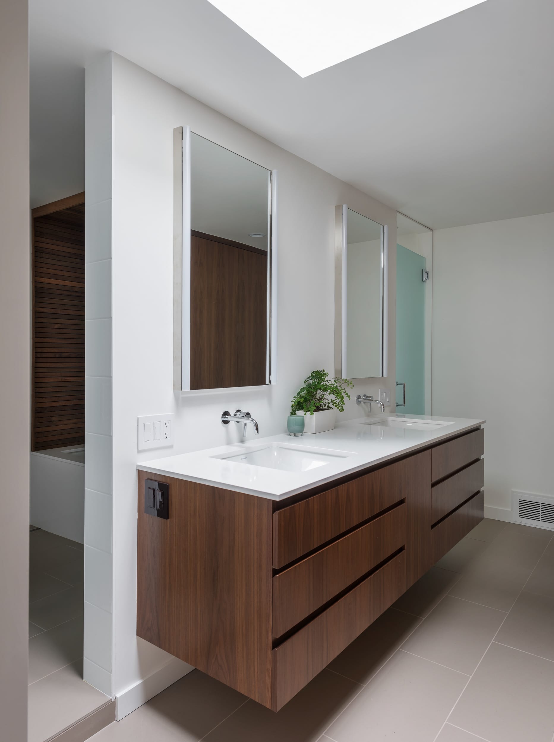 A modern bathroom with two sinks and a skylight.