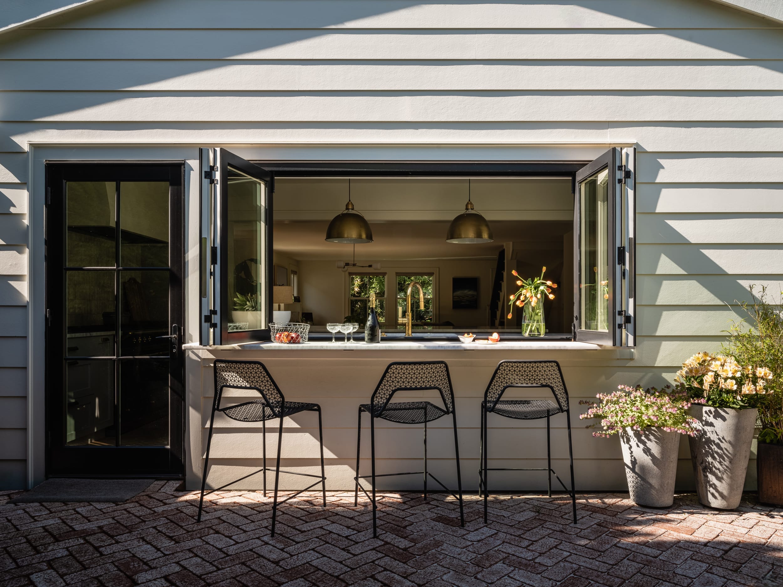 An outdoor kitchen with stools and a window.
