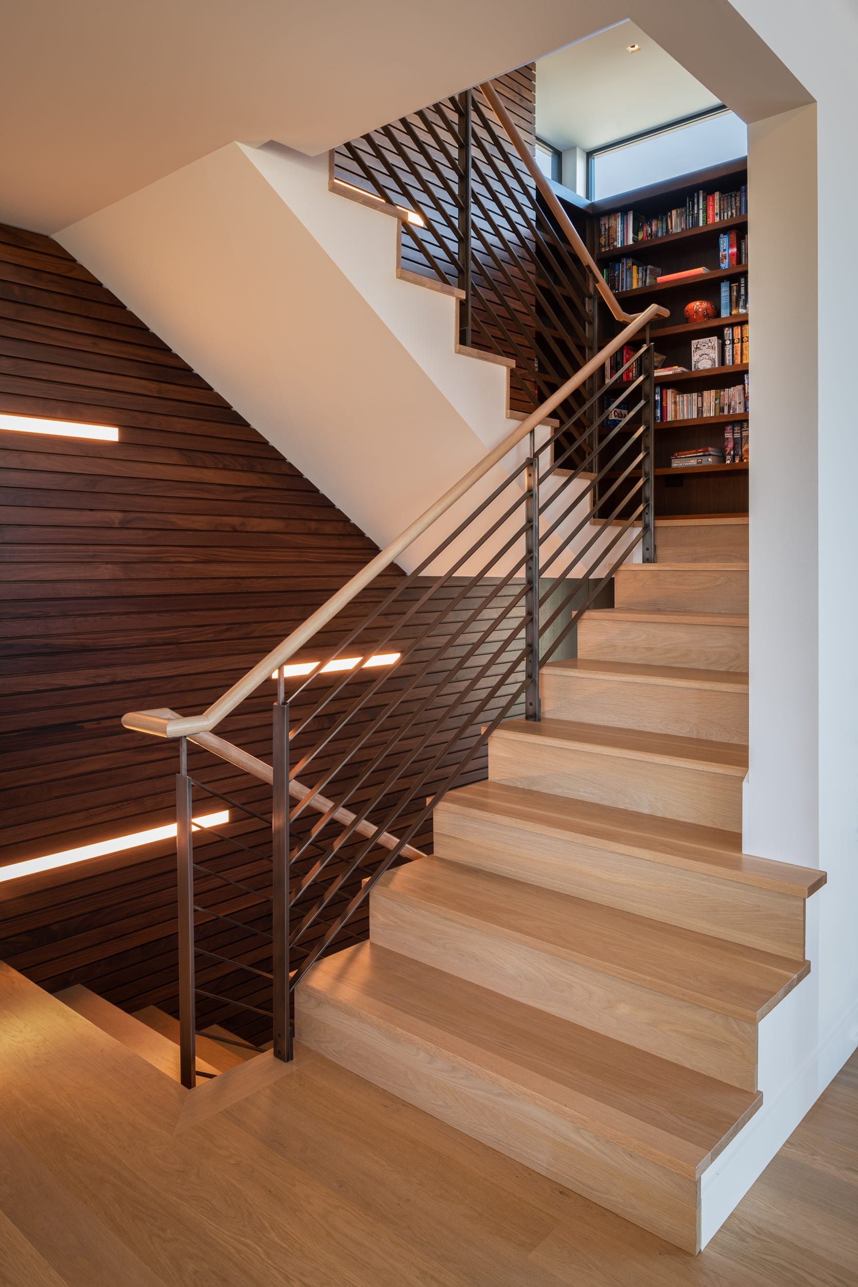 A modern staircase with wooden railings and bookshelves.