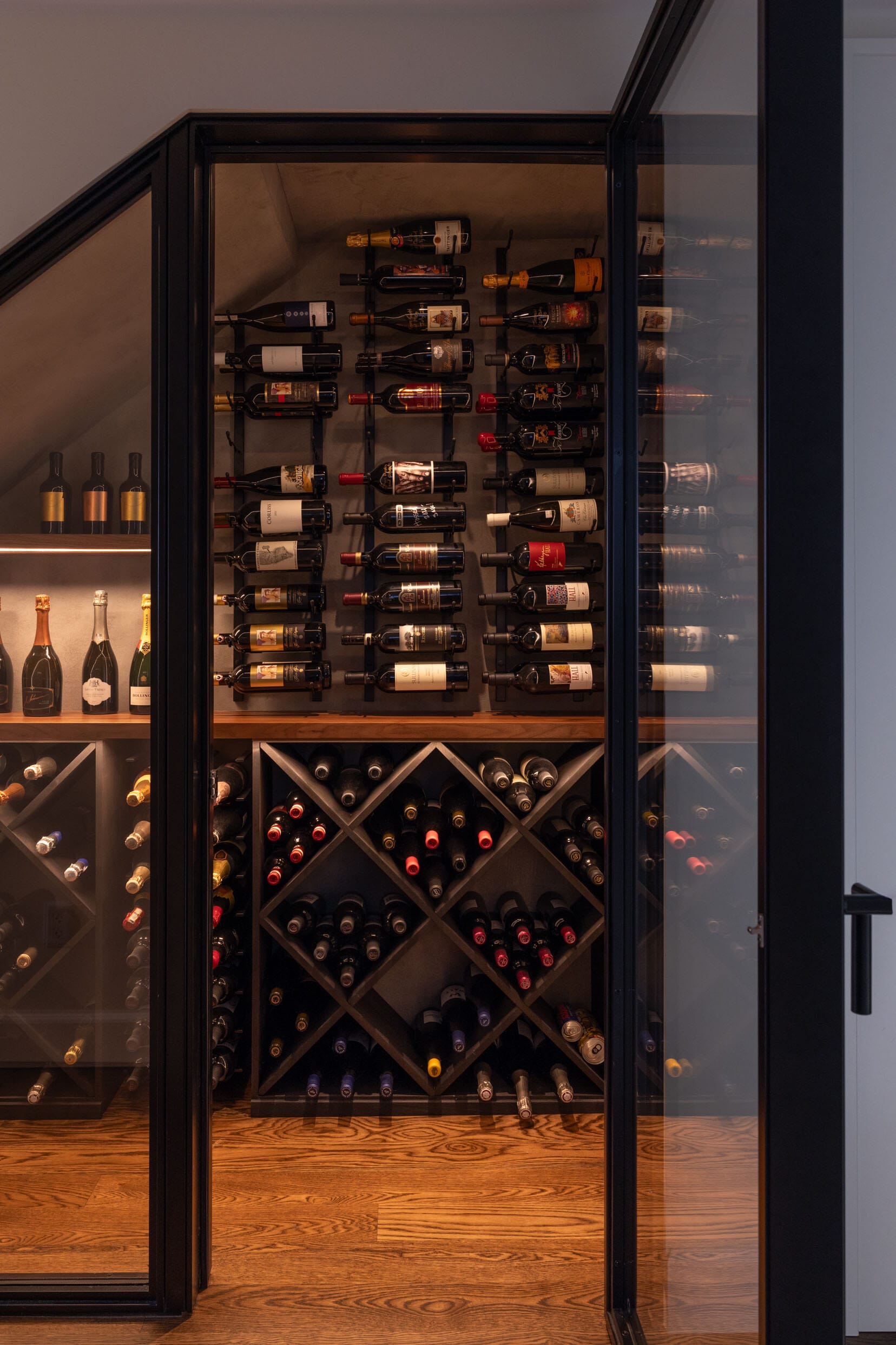 A glass-door wine cellar with neatly arranged wine bottles on wooden shelves and racks.