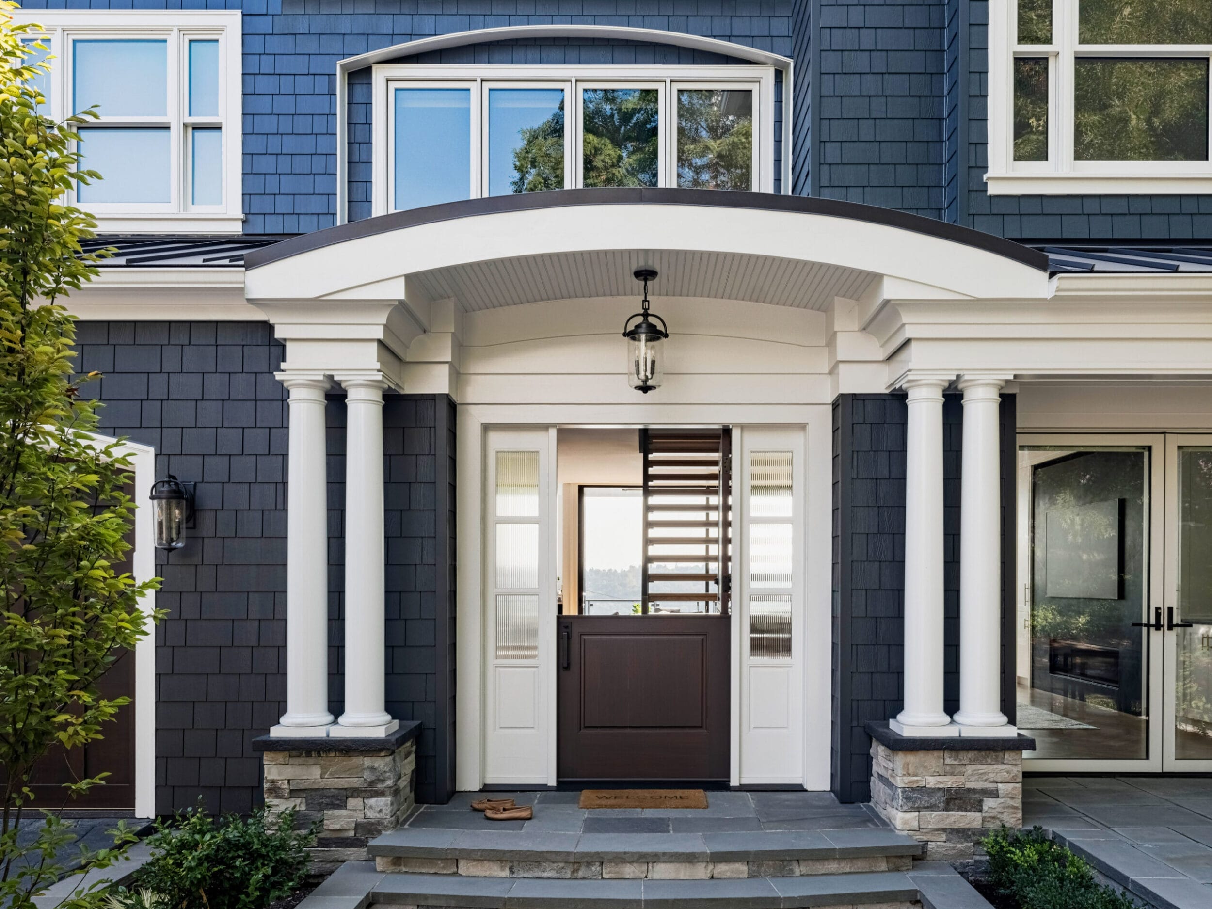 Front entrance of a house with a dark exterior, white columns, and a wooden door beneath an arched portico.