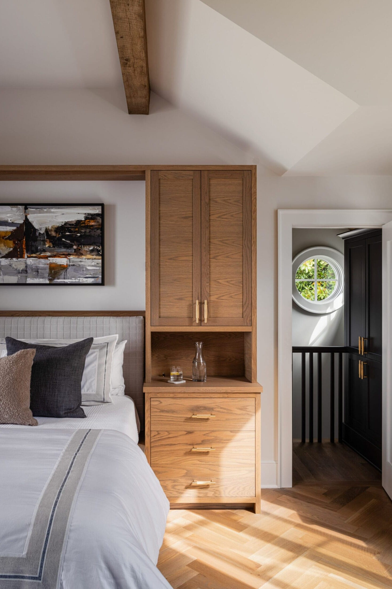 Bedroom with wood furniture, a bed with pillows, a painting on the wall, and a door leading to a hallway. Natural light illuminates the room.