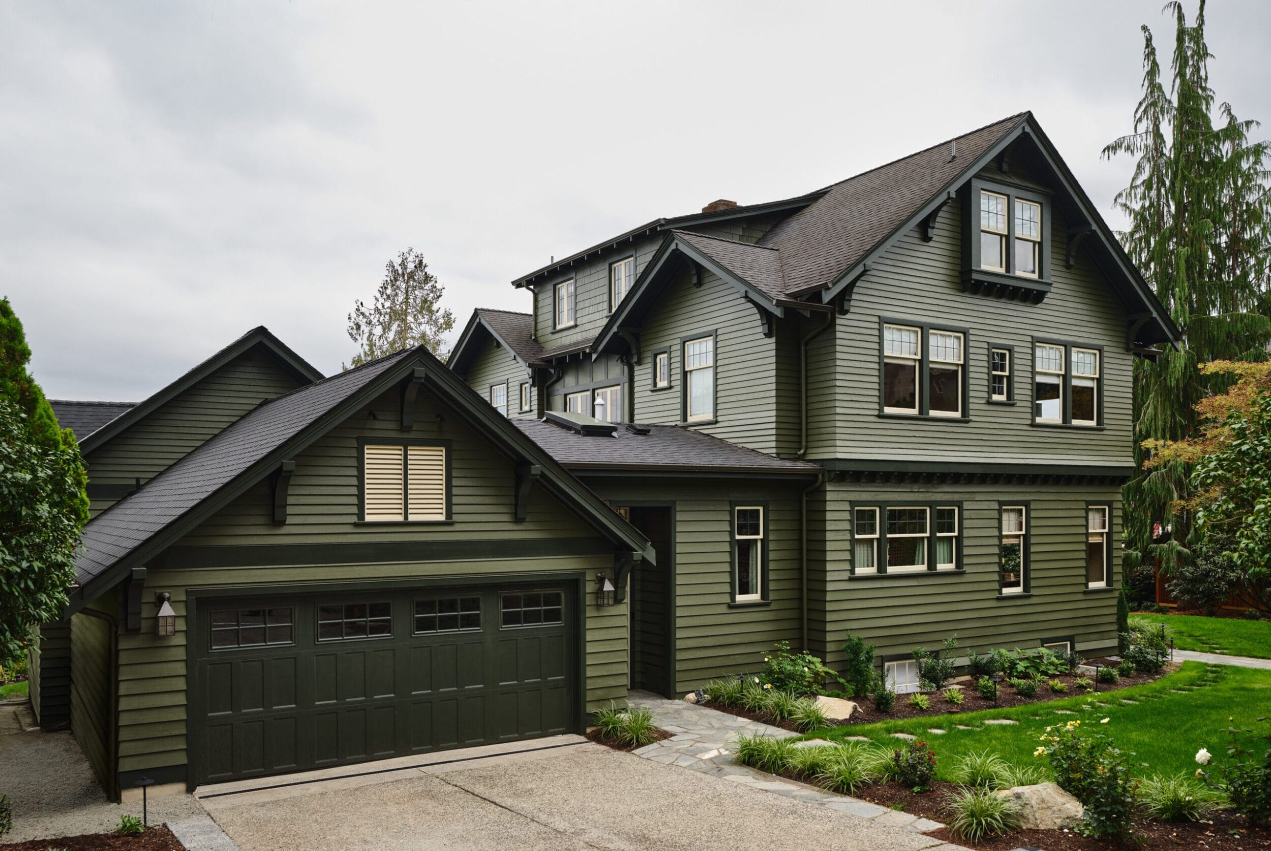 A two-story green house with a matching detached garage and landscaped front yard.