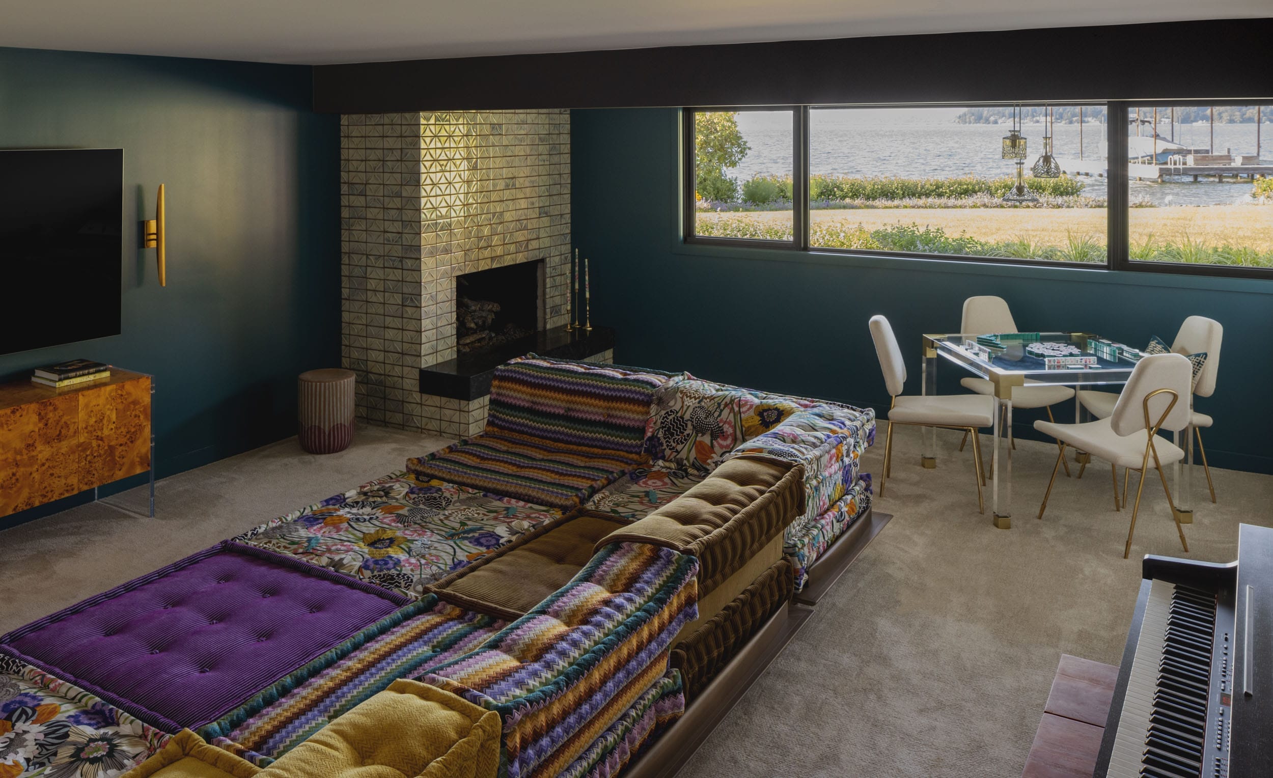 Living room with a colorful sectional sofa, brick fireplace, TV, and a window view of a lake. A small dining table with chairs is near the window.