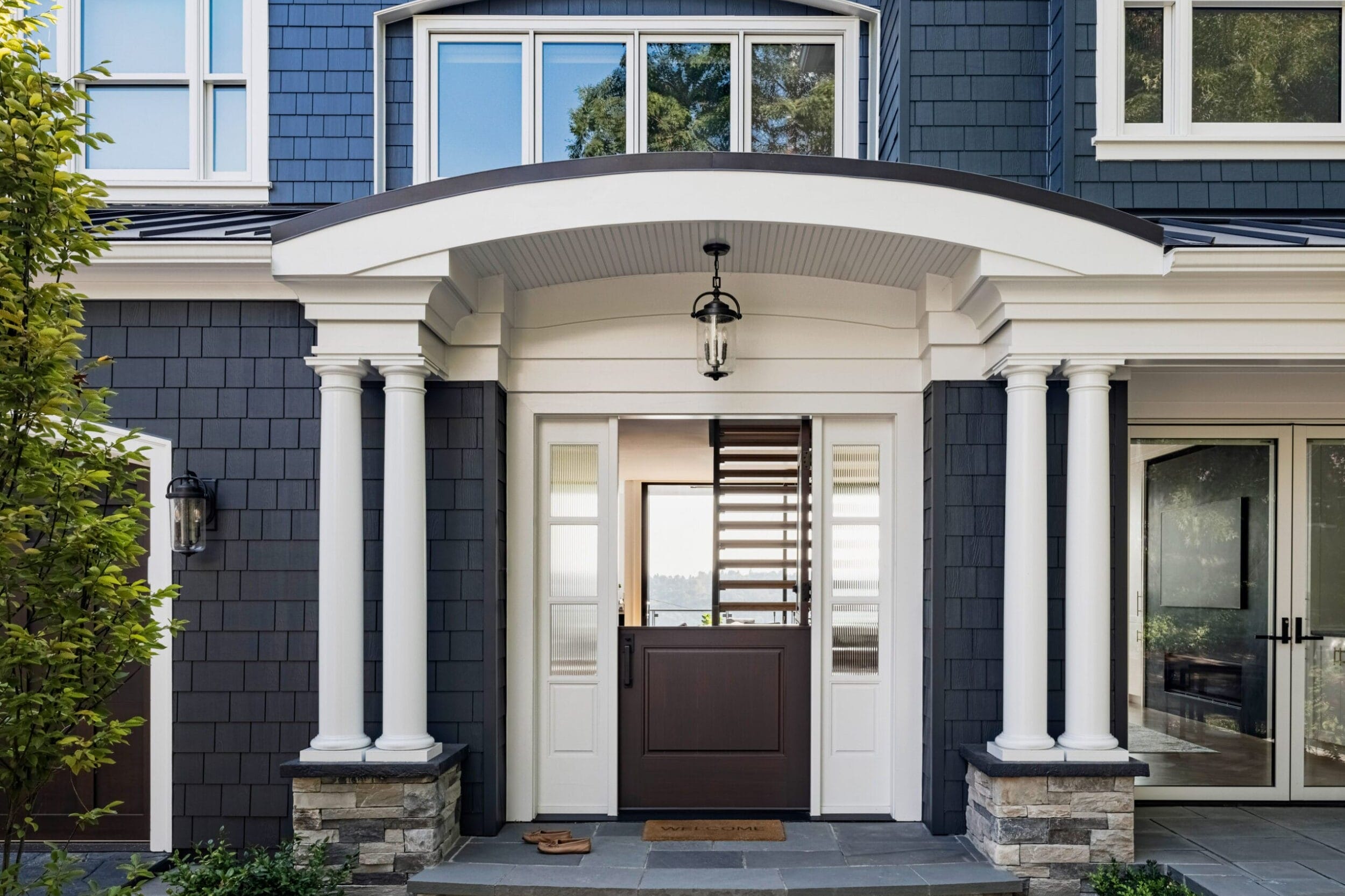 Elegant house entrance with a dark door, white columns, and a small hanging light. Steps lead to the door, framed by sidelights and windows above.