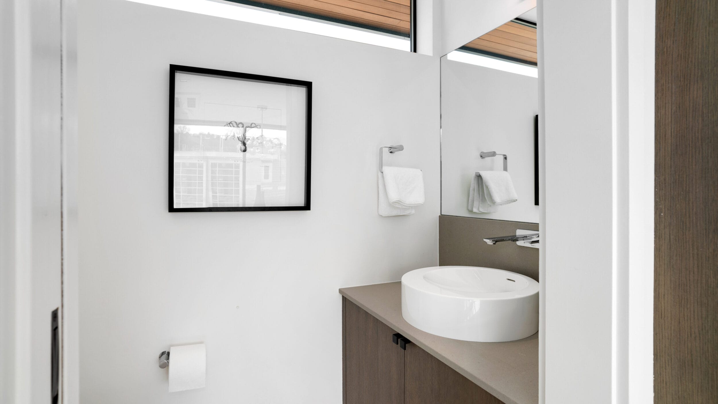 Minimalist bathroom with a wall-mounted sink, towel rings with folded towels, a framed picture, and a roll of toilet paper.