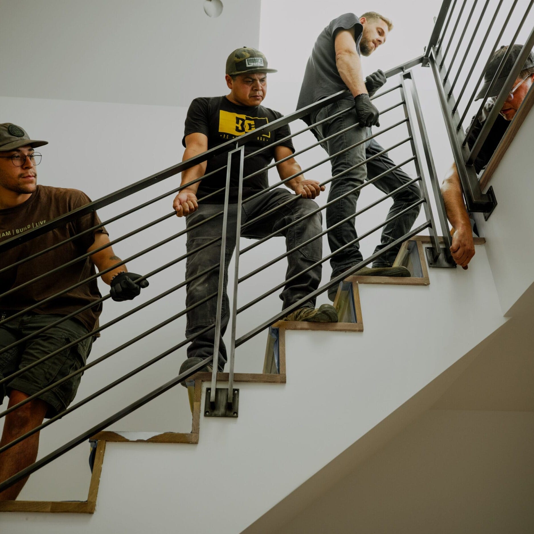 Four people work together to lift and install a metal stair railing inside a building by Dyna Metal Shop Seattle.