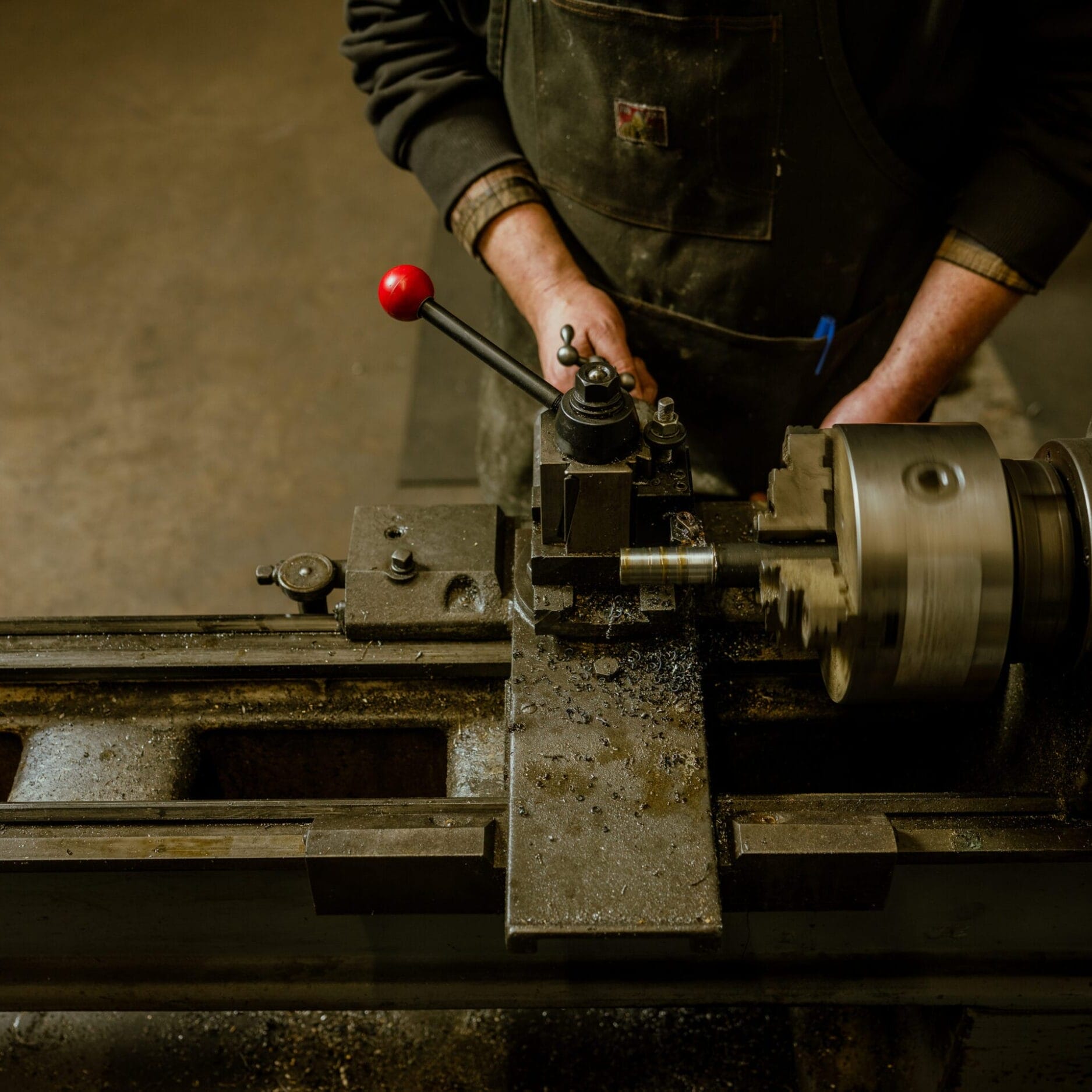 At Dyna Metal Shop Seattle, a person operates a metal lathe, skillfully shaping a cylindrical piece of metal as metal shavings scatter across the machine.