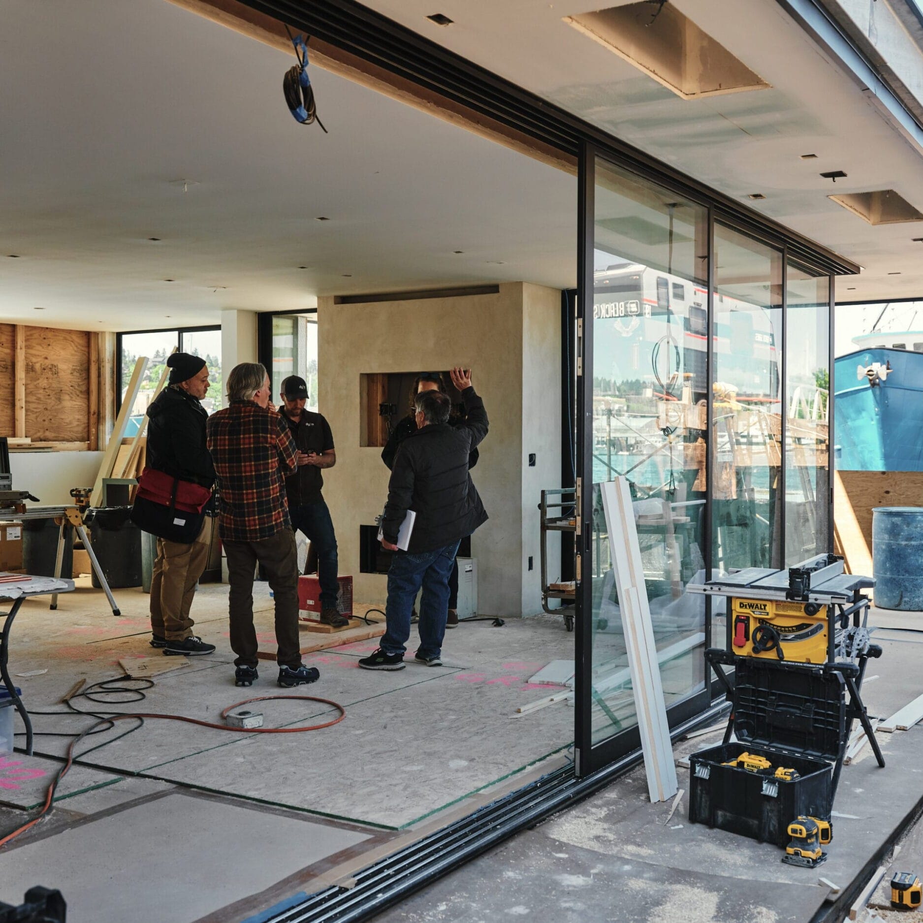 Four people discuss plans inside a partially finished building with construction tools and materials scattered throughout the site, consulting a Floating Homes Contractor about the next steps for their Seattle Floating Homes project.