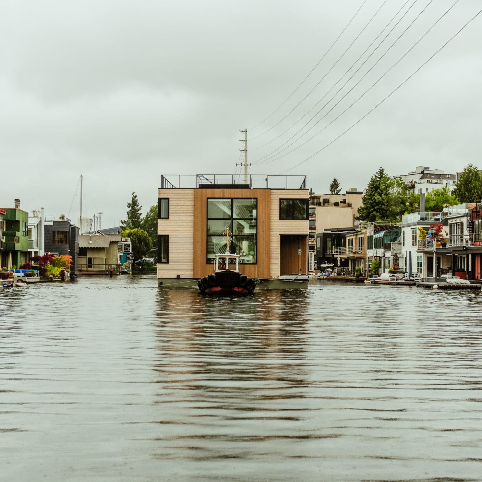 A canal lined with modern houseboats built by a skilled floating homes contractor, featuring small docks under a cloudy sky, with watercraft moored along both sides.